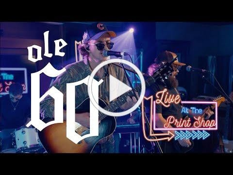 Live music performance at Hall of Fans print shop, featuring musicians, guitars, and vibrant stage lighting.