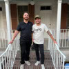 Graphic of two men standing on front porch of a house with white railing and brick steps.