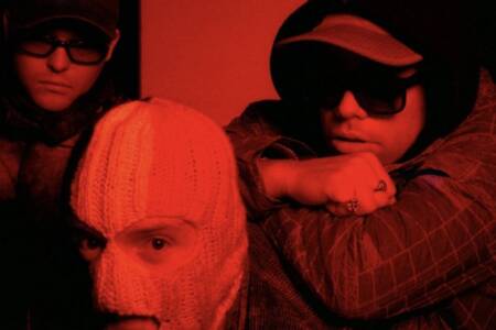 “Ya think it’s all poetry and clovers, when it’s raincoats and police Land Rovers. Salt of the earth, looking over their shoulder.” Kneecap share moody and intense new single Smugglers & Scholars