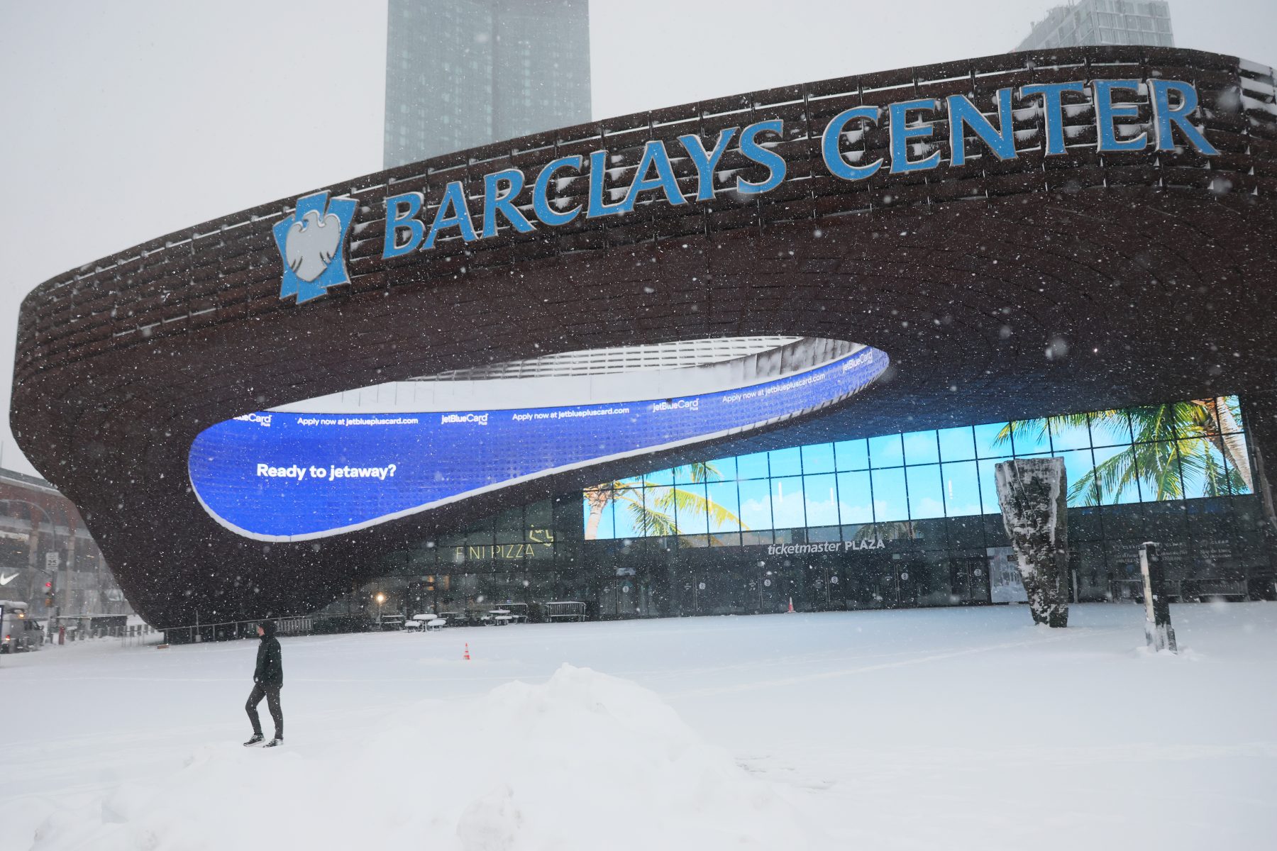 NEW YORK, NEW YORK - FEBRUARY 23: A person walks past the Barclays Center as snow falls during a blizzard on February 23, 2026 in Downtown Brooklyn in New York City. The northeast U.S. is bracing for an intense nor'easter with blizzard conditions, heavy snow, and strong winds. New York City Mayor Zohran Mamdani announced a state of emergency for NYC and issued a travel ban beginning at 9 p.m. tonight, and ending at 12 p.m. on Monday. NYC could get more than a foot of snow with up to two feet on Long Island and in parts of New Jersey. (Photo by Michael M. Santiago/Getty Images)