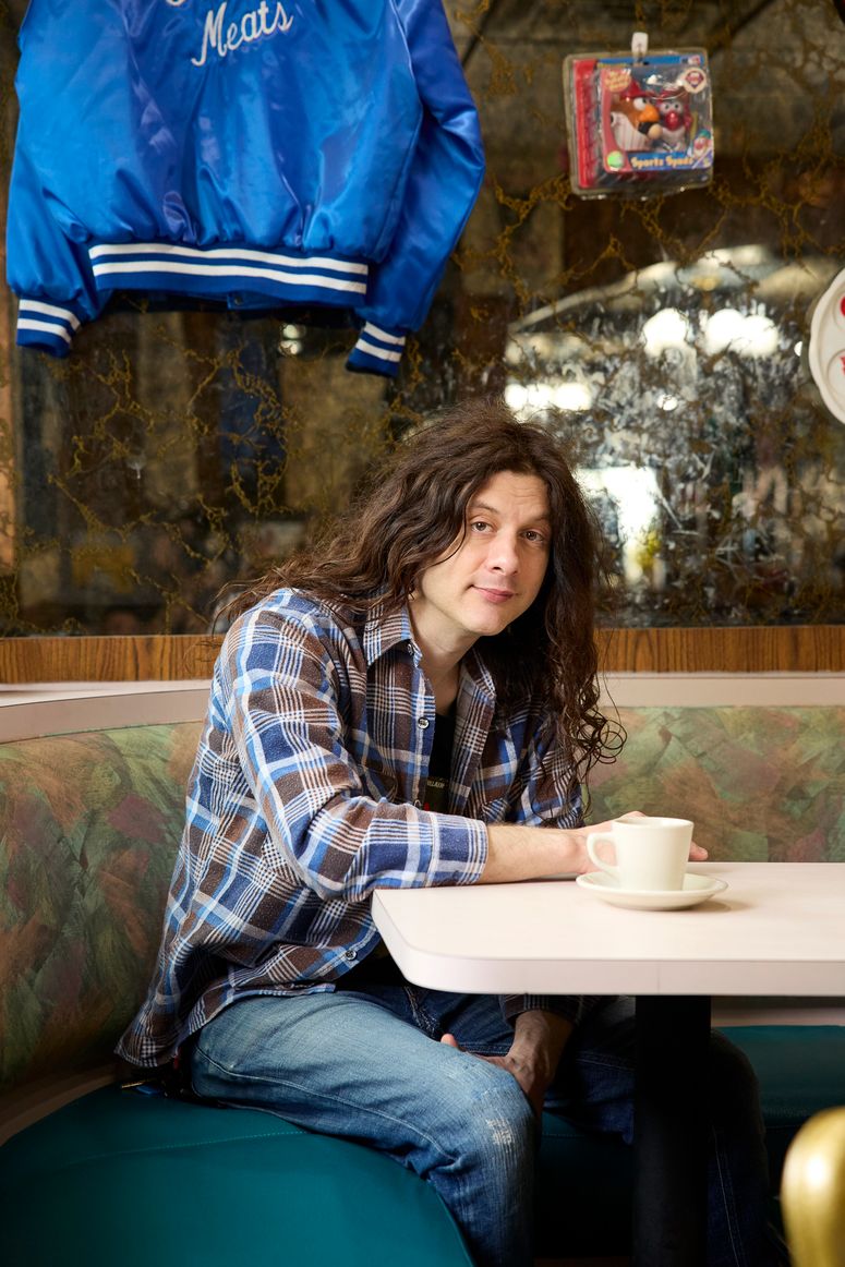 Image may contain: Kurt Vile, Person, Sitting, Face, Head, Photography, Portrait, Cup, Indoors, Restaurant, and Clothing